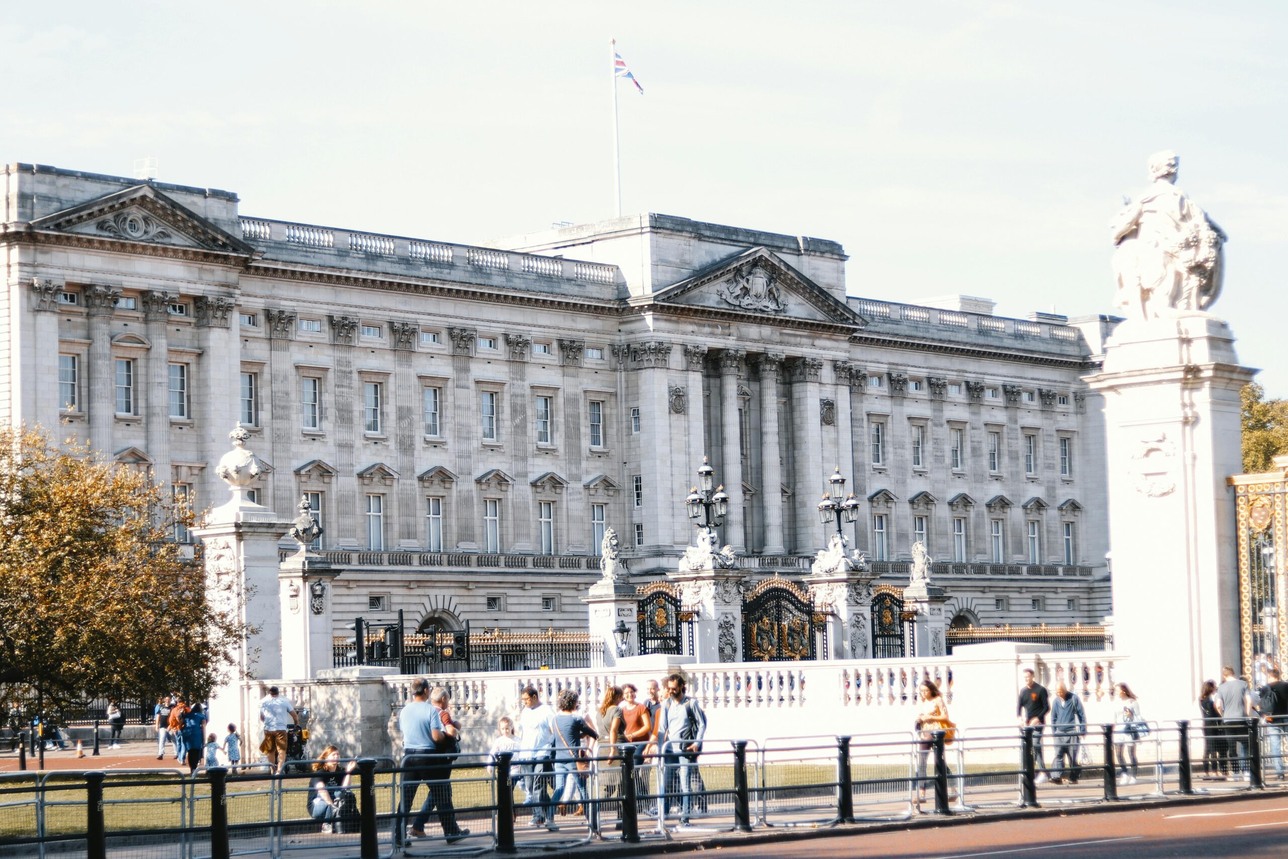 View of Buckingham Palace's facade with visitors in the foreground on a sunny day in London.