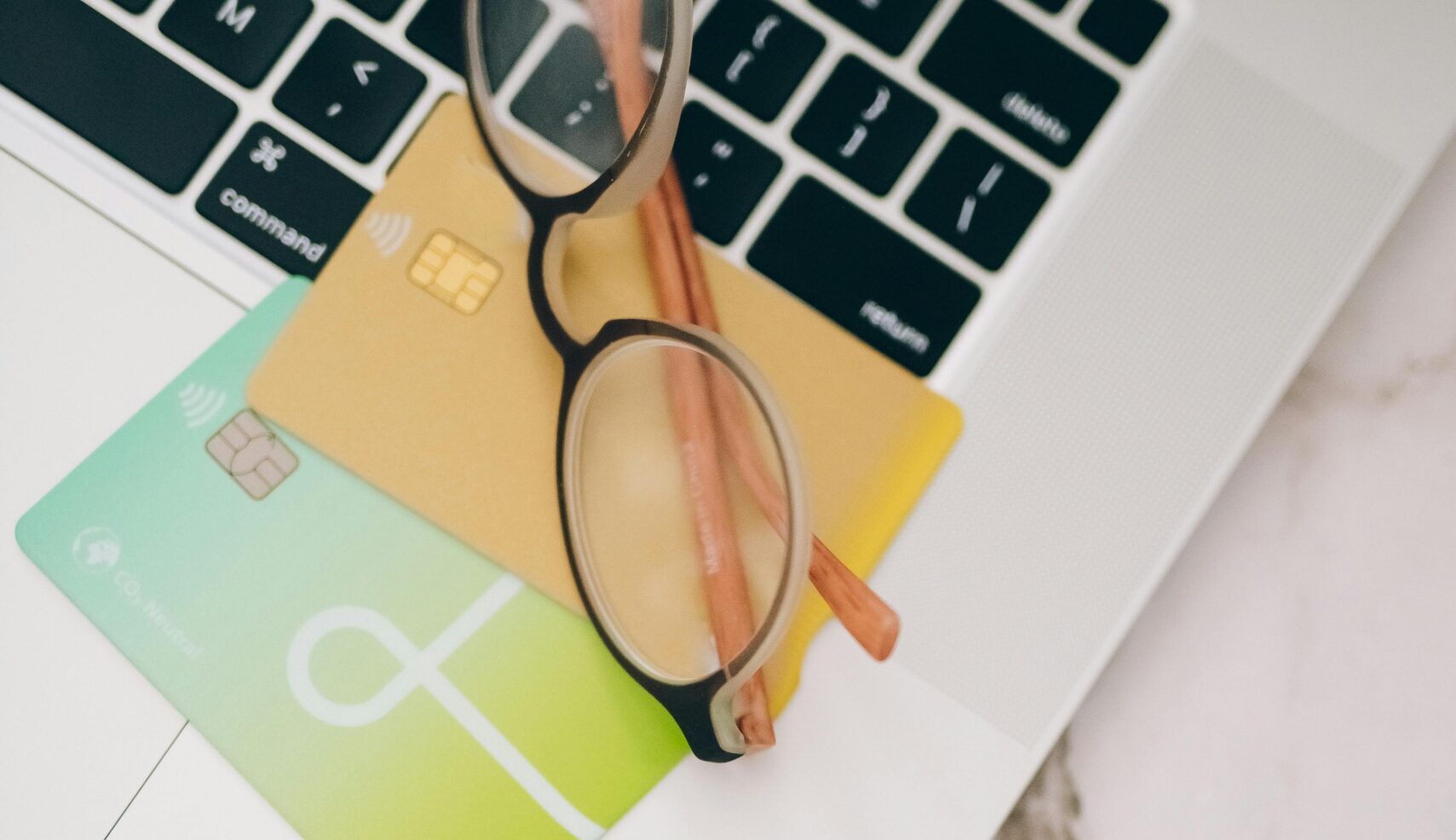 Eyeglasses and credit cards placed on a laptop keyboard for online work.