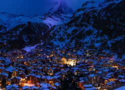 A captivating nighttime view of Zermatt, Switzerland, with illuminated houses and snow-covered mountains.