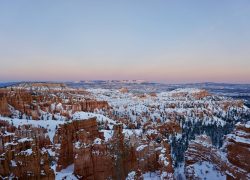 Stunning view of snow-capped hoodoos in Bryce Canyon National Park at sunrise, showcasing the park's rugged winter landscape.